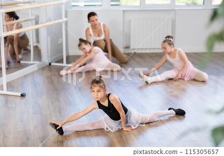During workout, girls sit on floor and do splits. 115305657