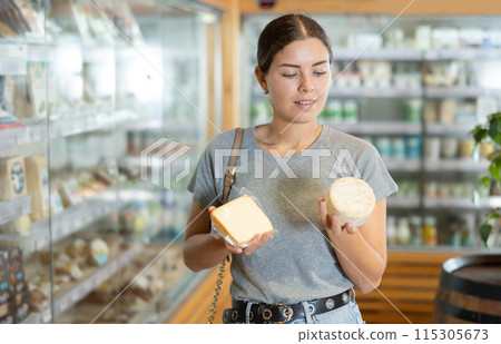 Girl in bio food store holds cheese of different varieties in hands and is thinking about buying Girl in bio food store holds cheese of different varieties in hands and is thinking about buying 115305673
