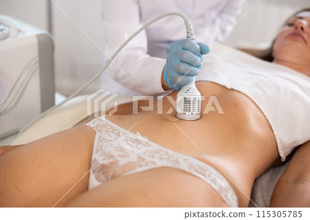Cosmetologist performing cryotherapy using cooling attachment on female client belly Cosmetologist performing cryotherapy using cooling attachment on female client belly 115305785