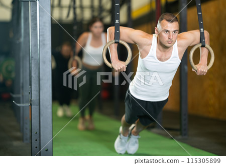 Man performing chest push-ups with gymnastic rings during workout in gym 115305899