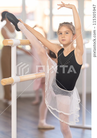 Ballet pose grand batman - little girls at a choreography lesson are learning ballet movements in studio 115305947