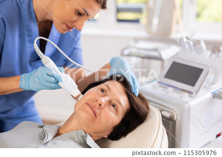 Mature woman undergoing hardware cosmetic facial treatment using ultrasonic shovel 115305976