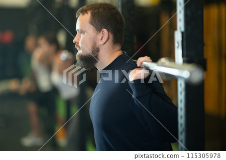 Determined young guy working out with weight rod during crossfit workout Determined young guy working out with weight rod during crossfit workout 115305978