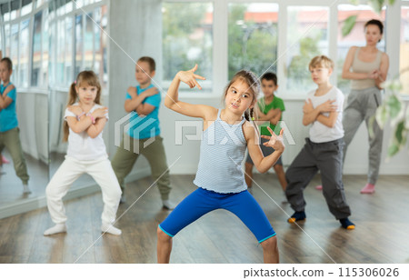 Positive juvenile girl engaged in breakdancing in training room with children's group Positive juvenile girl engaged in breakdancing in training room with children's group 115306026