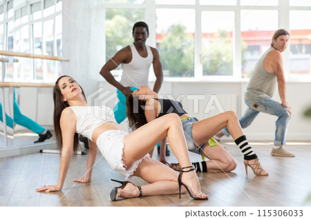 Girl in high heels sitting and lying on floor performing erotic dances during rehearsal with friends Girl in high heels sitting and lying on floor performing erotic dances during rehearsal with friends 115306033