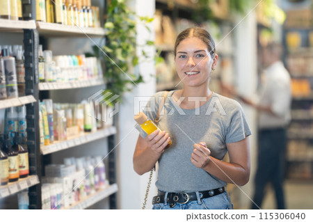 Positive young girl purchaser choosing cosmetic product in large supermarket 115306040