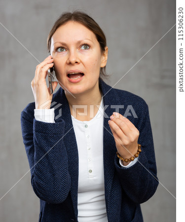 Indignant adult woman in jacket talking on phone 115306230