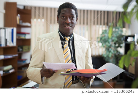 Excited african american businessman standing in office with papers Excited african american businessman standing in office with papers 115306242