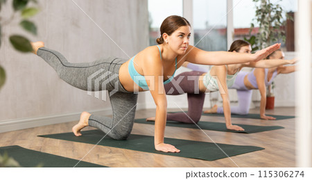Diligent women practicing balancing table pose of yoga in light fitness room 115306274