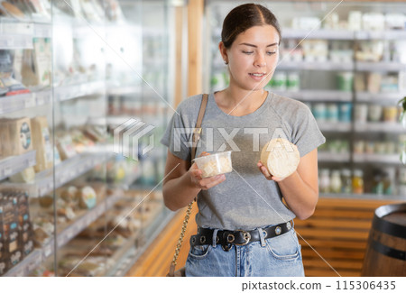 Positive young girl purchaser choosing cheese in large supermarket 115306435