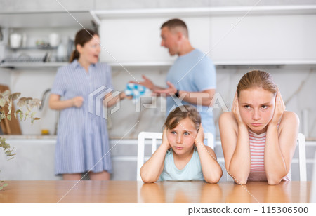 Frightened and frowning children sit at kitchen table during mom and dad quarrel. Frightened and frowning children sit at kitchen table during mom and dad quarrel. 115306500