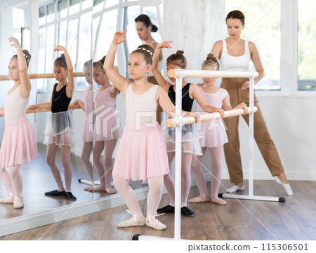 Teacher conducts class with children girls in ballet studio, observes doing grand plie exercise. 115306501