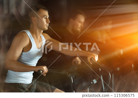 Stylized shot of determined man exercising on stationary bike in gym 115306575
