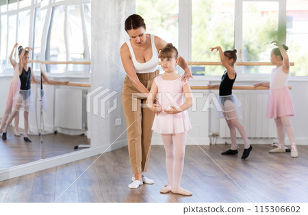 In studio, mentor corrects girls arm and leg, teaches correct dynamics and execution of movements 115306602