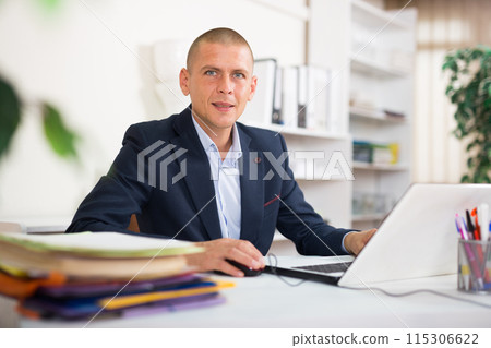 Portrait of business man working in office with laptop and documents Portrait of business man working in office with laptop and documents 115306622