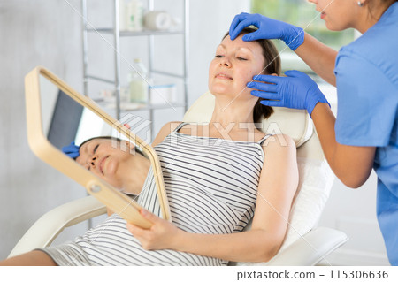 Young woman cosmetologists examines face of female patient Young woman cosmetologists examines face of female patient 115306636