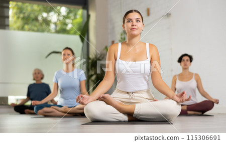 Young beautiful woman having yoga class sitting in lotus pose in yoga studio Young beautiful woman having yoga class sitting in lotus pose in yoga studio 115306691
