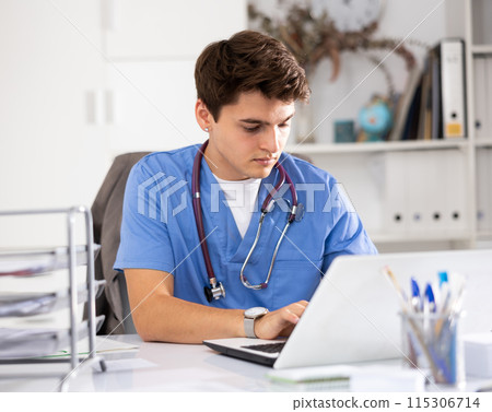 Focused doctor therapist works at a hospital computer, studying outpatient cards patients in resident office 115306714