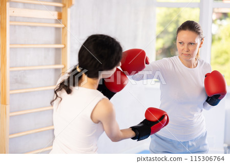 Focused woman practicing boxing punches in sparring during group self defence course Focused woman practicing boxing punches in sparring during group self defence course 115306764