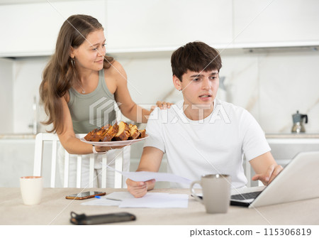 Young woman offering pie to guy working at laptop Young woman offering pie to guy working at laptop 115306819