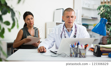 Doctor writing prescription to female patient on laptop at clinic 115306829
