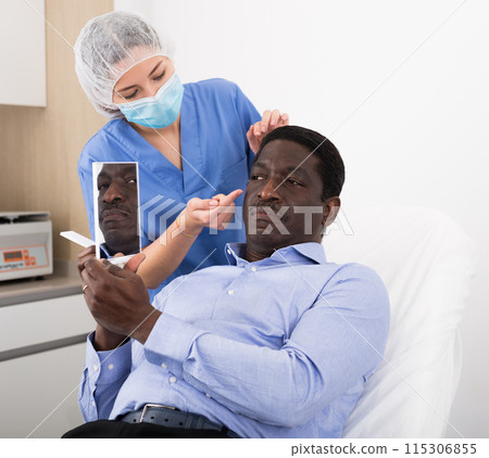 Cosmetologist examining male client face before procedure in clinic 115306855