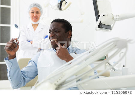 Man sitting and looking at mirror after tooth restoration in clinic Man sitting and looking at mirror after tooth restoration in clinic 115306978