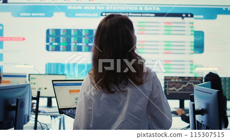 Project leader conducting a market research with a big screen in company headquarters office, ensuring enterprise progress. Financial manager studying the current organizational situation. Camera B. 115307515
