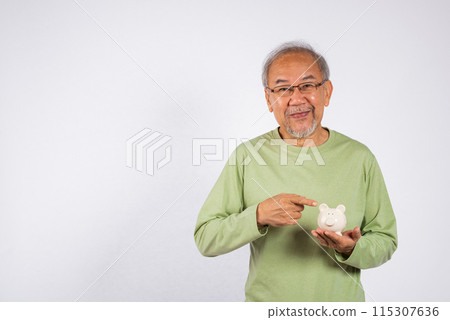 Portrait Asian older man points to a white piggy bank holding on hand studio shot isolated on white background. Concept of responsibility and financial planning, Saving money After retirement Portrait Asian older man points to a white piggy bank holding on hand studio shot isolated on white background. Concept of responsibility and financial planning, Saving money After retirement 115307636