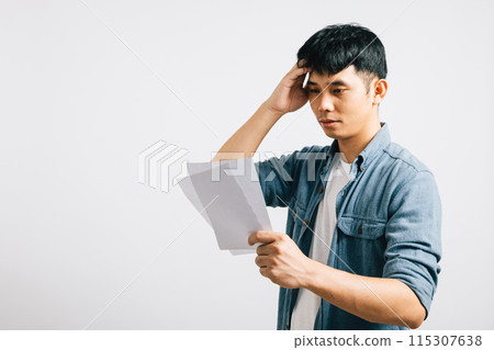 In a studio shot on white, a troubled Asian man holds a paper, calculating bills and displaying signs of financial strain, portraying his upset and stress over the situation. over bill In a studio shot on white, a troubled Asian man holds a paper, calculating bills and displaying signs of financial strain, portraying his upset and stress over the situation. over bill 115307638