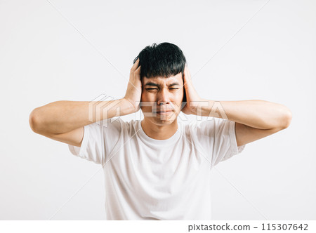 An Asian man in pain, using his hands to cover his ears and shutting his eyes to cope with the loud noise. Studio shot isolated on white background, showing his need for relief. An Asian man in pain, using his hands to cover his ears and shutting his eyes to cope with the loud noise. Studio shot isolated on white background, showing his need for relief. 115307642