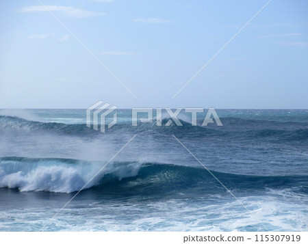 Waves break and crash towards the shore with dramatic blue sky Waves break and crash towards the shore with dramatic blue sky 115307919