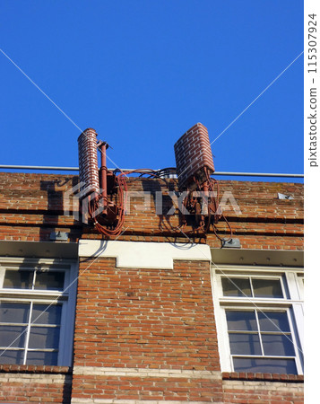 Cellular antenna painted to look like red bricks mounted to the top of red brick wall 115307924