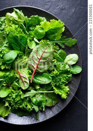 A mix of fresh raw salad greens on a black plate 115308081