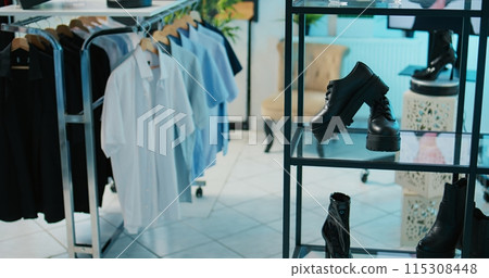 Empty modern clothing store filled with formal wear designs, retail shop with fashion items on hangers and racks. Shopping center boutique with trendy accessories and shoes on display. Camera B. Empty modern clothing store filled with formal wear designs, retail shop with fashion items on hangers and racks. Shopping center boutique with trendy accessories and shoes on display. Camera B. 115308448