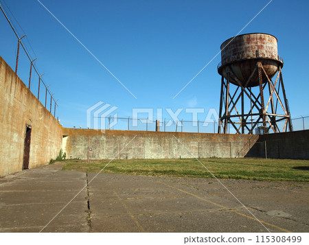 Rusting water tower stands beyond the wall  and bard wire fence 115308499
