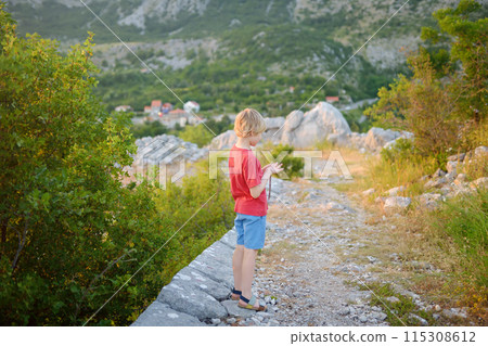Preteen boy hiking in mountains near Fort Kosmach in Montenegro. Fortress is located near Budva. Old castle was built as defensive structure and observation post. Sights of Montenegro. Preteen boy hiking in mountains near Fort Kosmach in Montenegro. Fortress is located near Budva. Old castle was built as defensive structure and observation post. Sights of Montenegro. 115308612