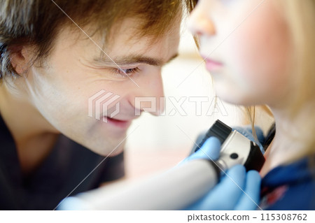 A caring doctor checks moles on the skin of a small child. A dermatologist looks at a rash on the chest of a girl using a dermatoscope. A caring doctor checks moles on the skin of a small child. A dermatologist looks at a rash on the chest of a girl using a dermatoscope. 115308762