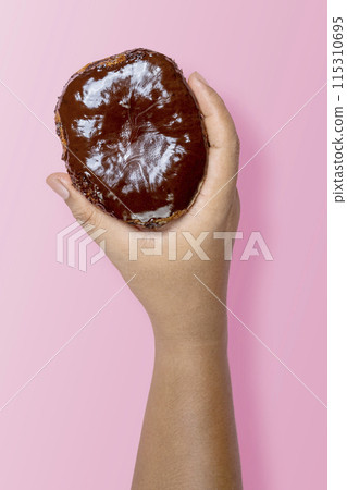 A human hand holding a delicious donut with a chocolate sprinkle decoration 115310695
