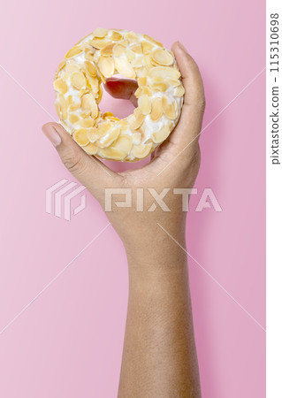 Hand holding a white almond donut on pink background 115310698