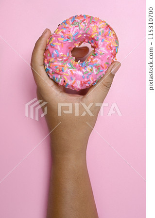 Human hand holding a delicious donut with a colorful sprinkle decoration Human hand holding a delicious donut with a colorful sprinkle decoration 115310700