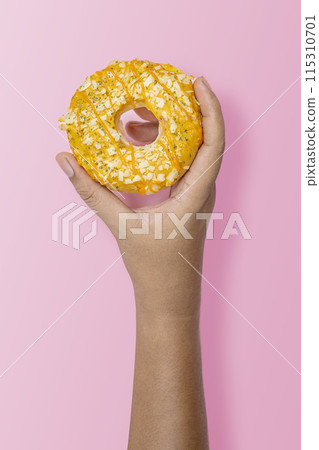 Hand holding a sprinkled donut on pink background Hand holding a sprinkled donut on pink background 115310701