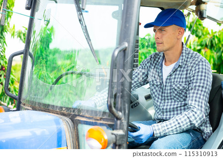Skilled male farmer working on farm tractor in orchard 115310913