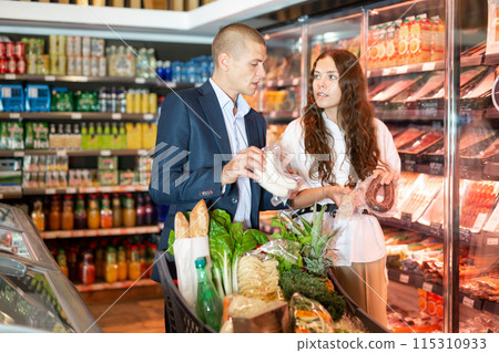 Glad couple is standing with cart with products in supermarket Glad couple is standing with cart with products in supermarket 115310933