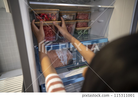 A little girl arranges a snack container on the refrigerator 115311001