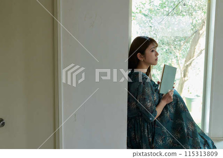 A woman reading a book at the window side A woman reading a book at the window side 115313809