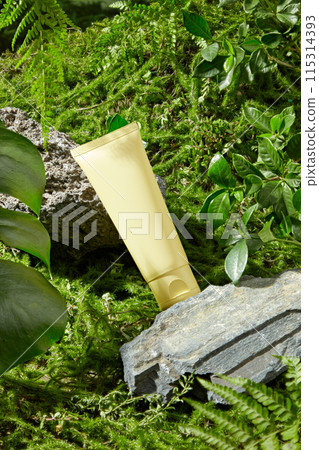 Cosmetic advertising mockup from high angle shot with nature theme, an unbranded yellow cosmetic tube lays on two pedestal of stone, the green grass below. Blank space for adding text 115314393