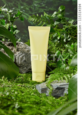 Advertising photo for cosmetic product, which made from natural ingredient. In the middle of frame has a blank label yellow tube featured, a stone podium in front, surrounded green plants 115314394