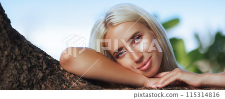 Blonde Woman Resting Head on Tree Branch Outdoors Blonde Woman Resting Head on Tree Branch Outdoors 115314816