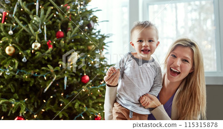 Portrait, baby and happy with mother in living room, holding hands for love and christmas holiday. Smile, motherhood and toddler by woman together, hug and play by sitting for relationship at home Portrait, baby and happy with mother in living room, holding hands for love and christmas holiday. Smile, motherhood and toddler by woman together, hug and play by sitting for relationship at home 115315878